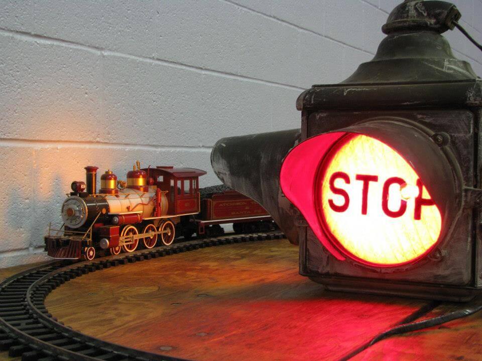 red model toy train on tracks passing a giant red stop light